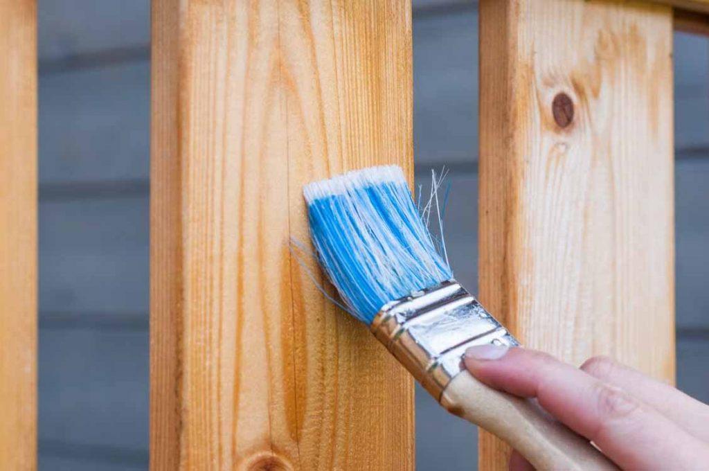 Brush applying fresh paint to a timber deck rail during an exterior repaint
