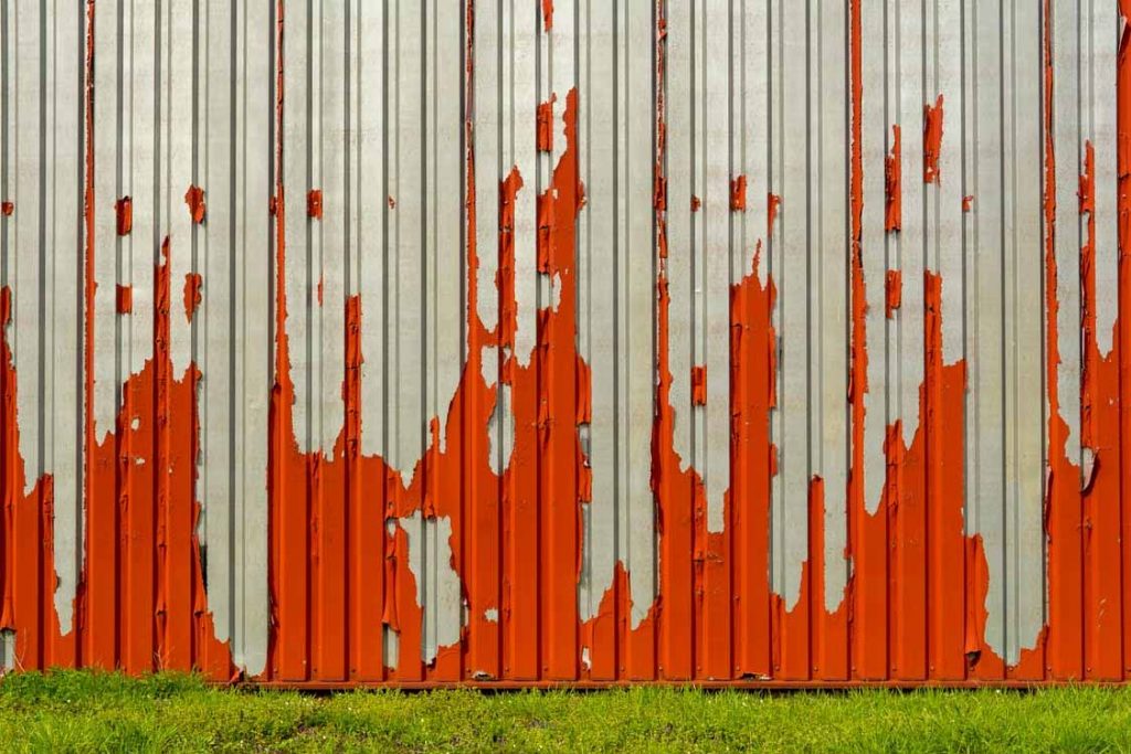 Old paint peeling off corrugated metal cladding before stripping and repainting